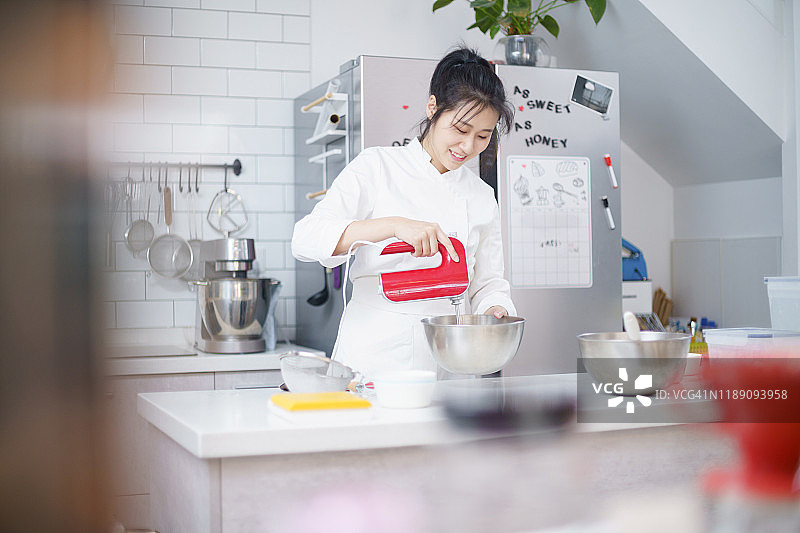 年轻的亚洲女性用搅拌器在碗里混合蛋糕面团图片素材