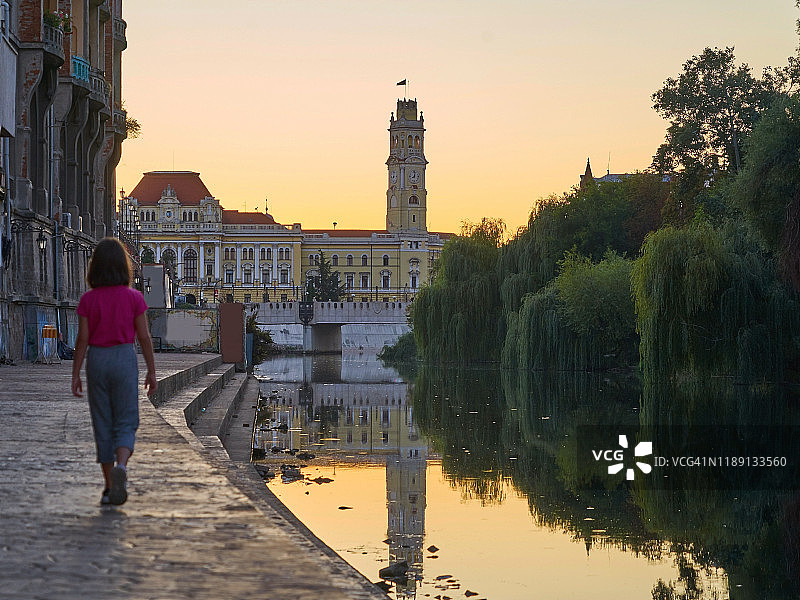 9岁女孩在中世纪背景下，傍晚在罗马尼亚克拉约瓦市的河边散步图片素材