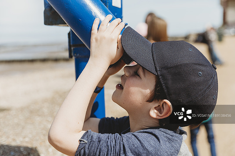 男孩戴着帽子在海滩上用望远镜观察图片素材