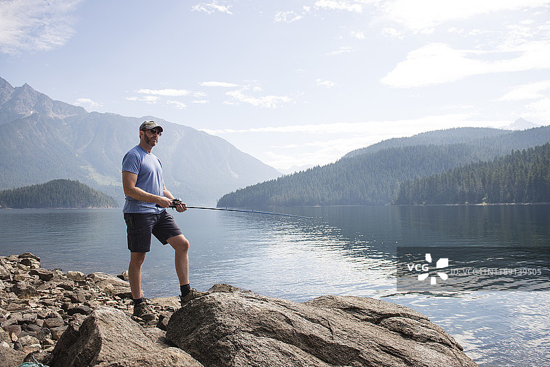男人站在华盛顿州罗斯湖的岩石上钓鱼图片素材