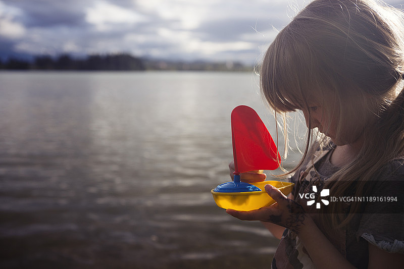 儿童在巴伐利亚湖边手持红色帆船塑料玩具船图片素材
