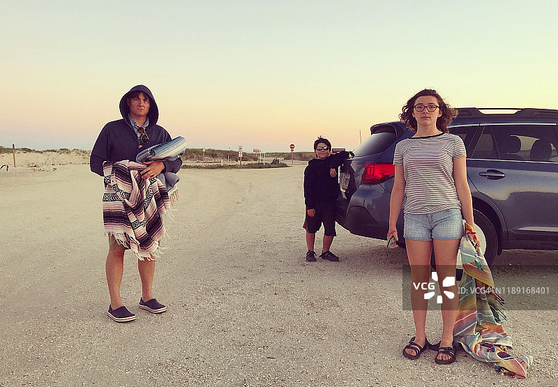 海滩上的一家人打开汽车后备箱，盖着毯子的幽默肖像图片素材