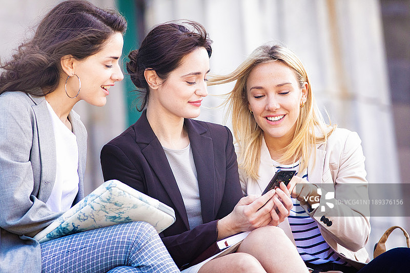 女大学生通过手机向她的两个朋友展示一个想法图片素材