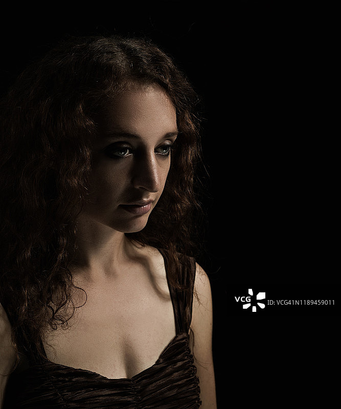 长波浪黑发年轻女子四分之三视图，身穿棕色无袖褶皱衬衫，表情茫然，深色工作室灯光图片素材
