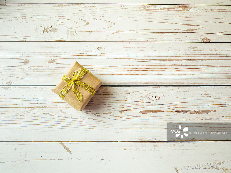 白色木桌上带有棕色再生纸和金色蝴蝶结的礼品包装图片素材