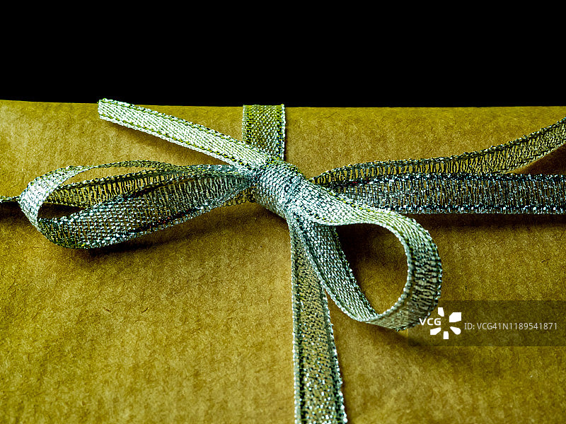 黑色背景上的棕色再生纸银色蝴蝶结礼品包装图片素材