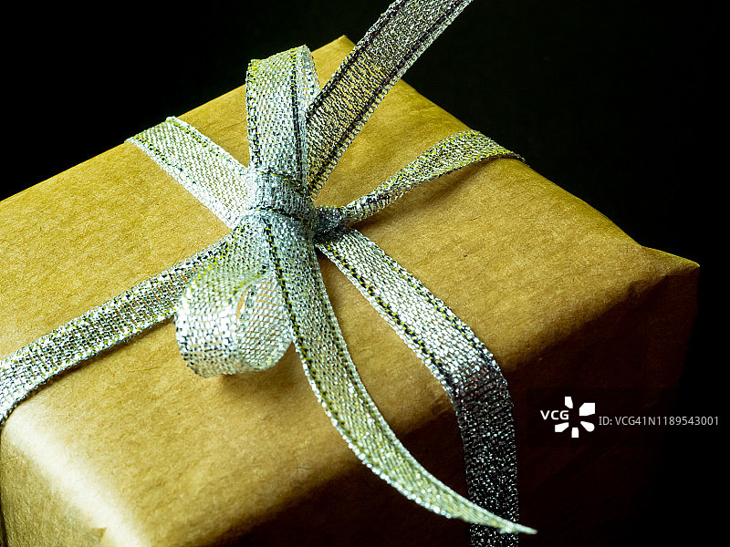 黑色背景上的棕色再生纸银色蝴蝶结礼品包装图片素材