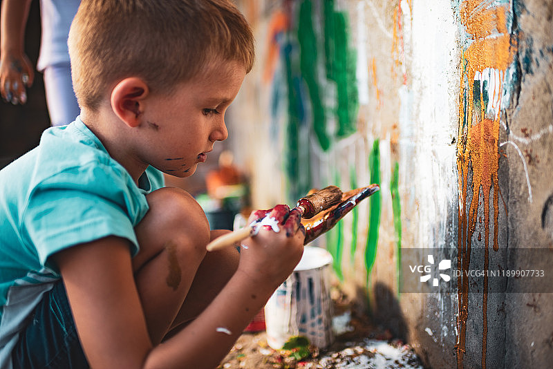 快乐的小男孩在墙上开心地涂鸦。图片素材