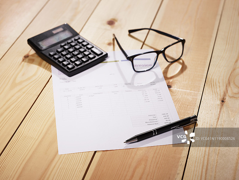 木桌上的发票、眼镜、笔和计算器图片素材