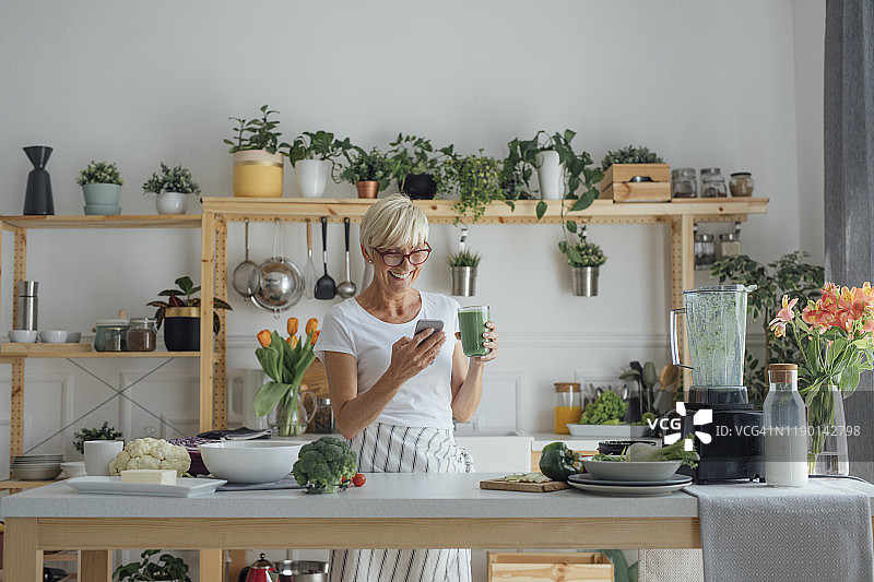 在厨房使用手机的中年妇女图片素材
