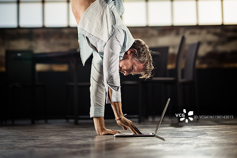 中年男人边做倒立边用笔记本电脑打字图片素材