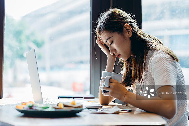 抑郁的年轻亚裔女子在咖啡馆喝咖啡时头痛图片素材