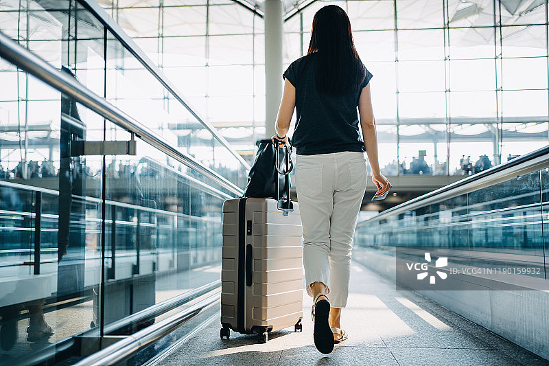 年轻亚洲女子携带行李箱在机场候机大厅的后视图图片素材