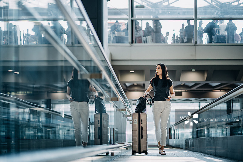手持护照，拉着行李箱的年轻亚洲女性走在机场大厅里图片素材