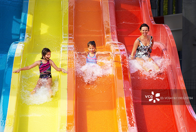 幸福家庭，母亲和两个女儿在水上乐园尖叫着滑下滑梯图片素材