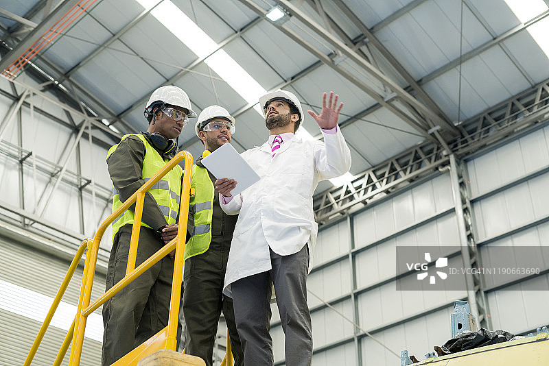 三名拉丁裔男子出现在黄色楼梯上，其中两名是机械师，一名是工程师。三个人似乎在看着工程师给他们展示的东西。图片素材