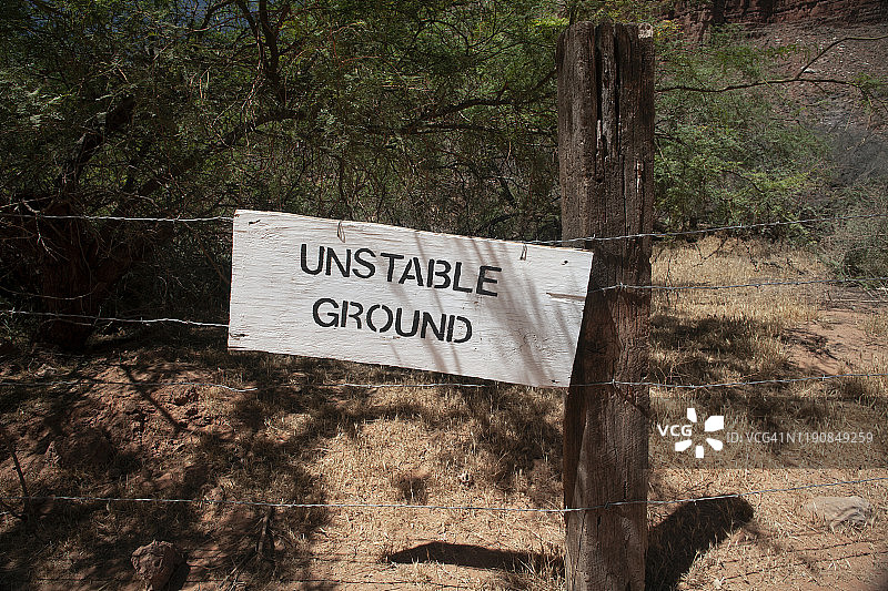 警告地面不稳定的木制标牌，连接到带刺铁丝网上图片素材
