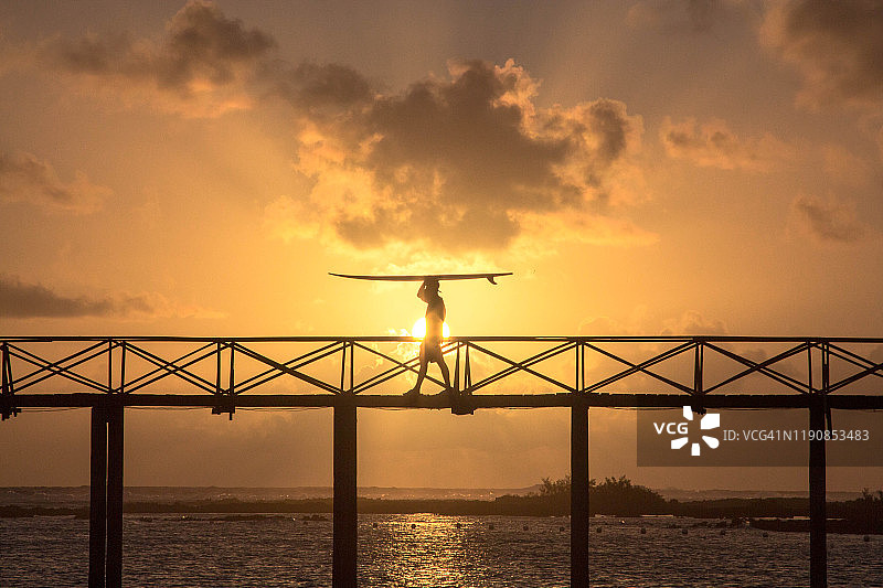 男人在云九锡亚高菲律宾桥上扛着冲浪板图片素材