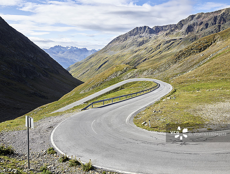 阳光明媚的日子里，蜿蜒的山路通往多云的天空，奥地利蒂罗尔州图片素材
