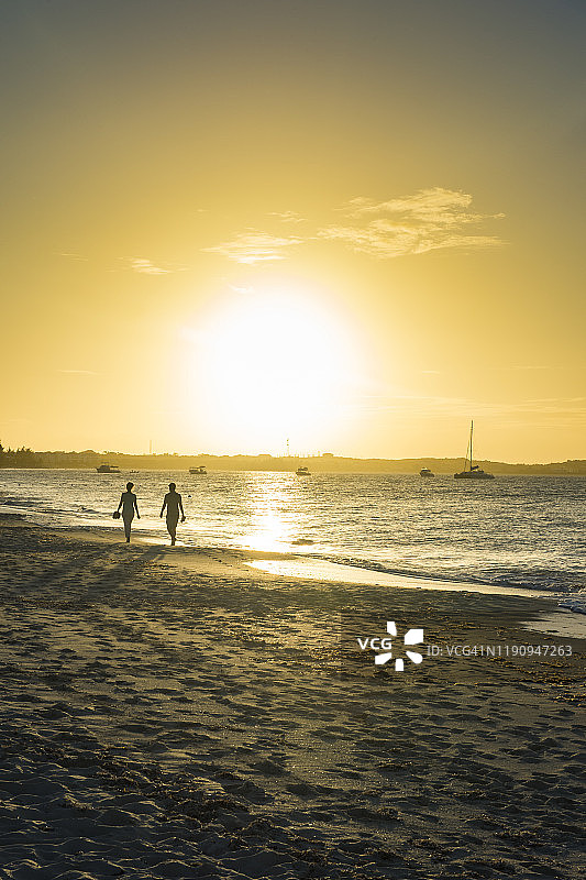 日落时，情侣在特克斯和凯科斯群岛普罗维登西亚莱斯岛格雷斯湾海滩散步的剪影图片素材