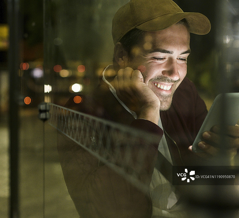 在葡萄牙里斯本，夜晚坐在巴士站使用手机的欢笑青年 портрет图片素材