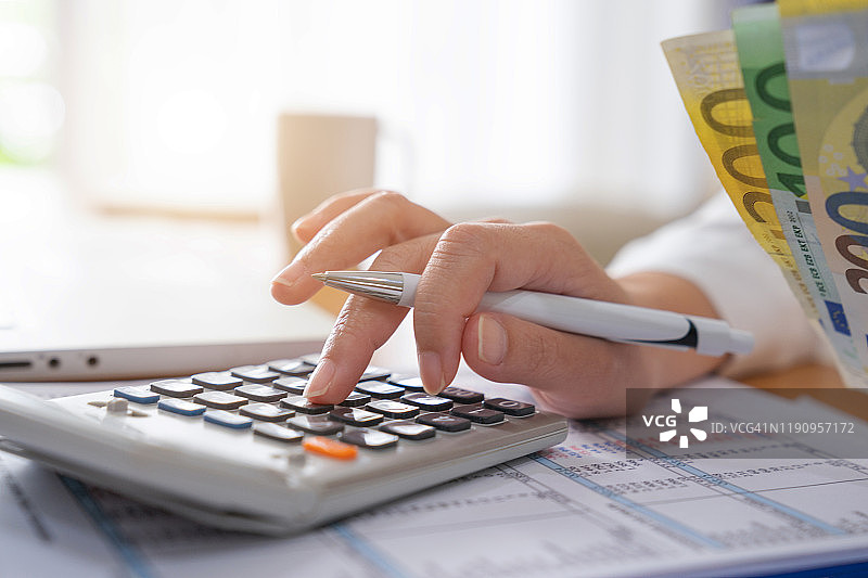 商务女性在家办公时使用电脑和计算器，并在笔记本上记录一些数据以计算财务图片素材