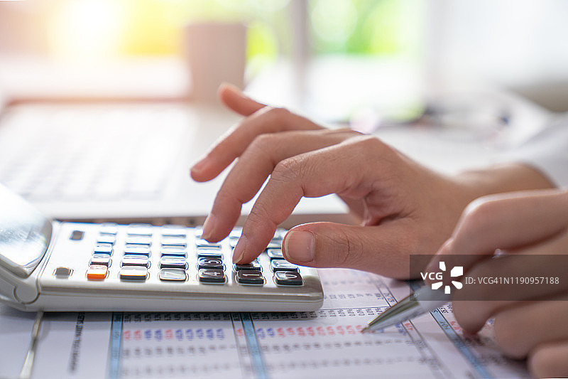 商务女性在家办公时使用电脑和计算器，并在笔记本上记录一些数据以计算财务图片素材