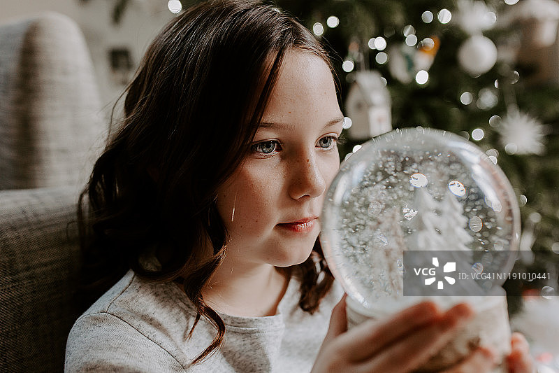 女孩坐在圣诞树旁，望着水晶球图片素材