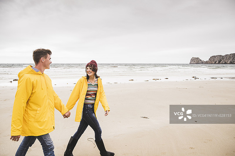 年轻女子身穿黄色雨衣在法国布列塔尼海滩散步图片素材