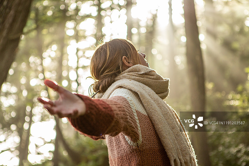 年轻女子在阳光照耀的雨林中拥抱树木图片素材