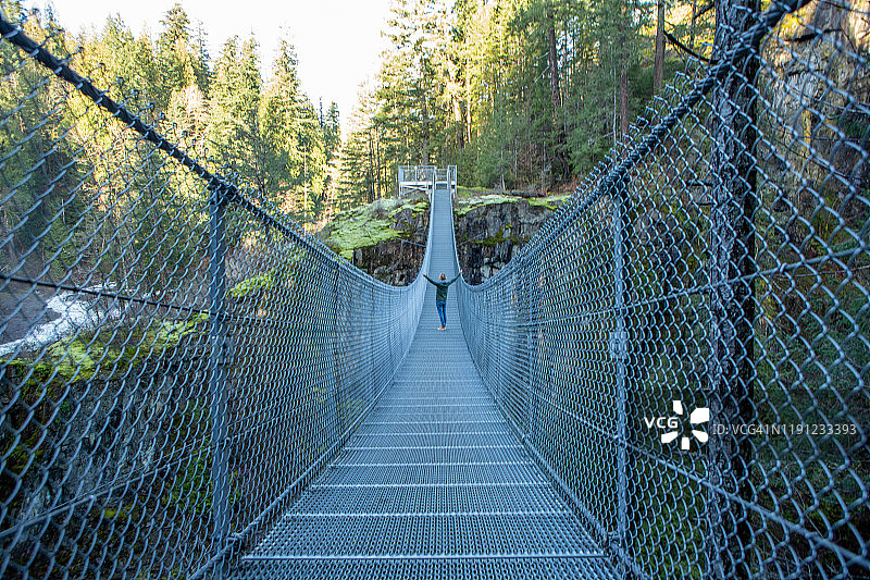 在加拿大热带雨林峡谷中伸开双臂走过吊桥的男人图片素材