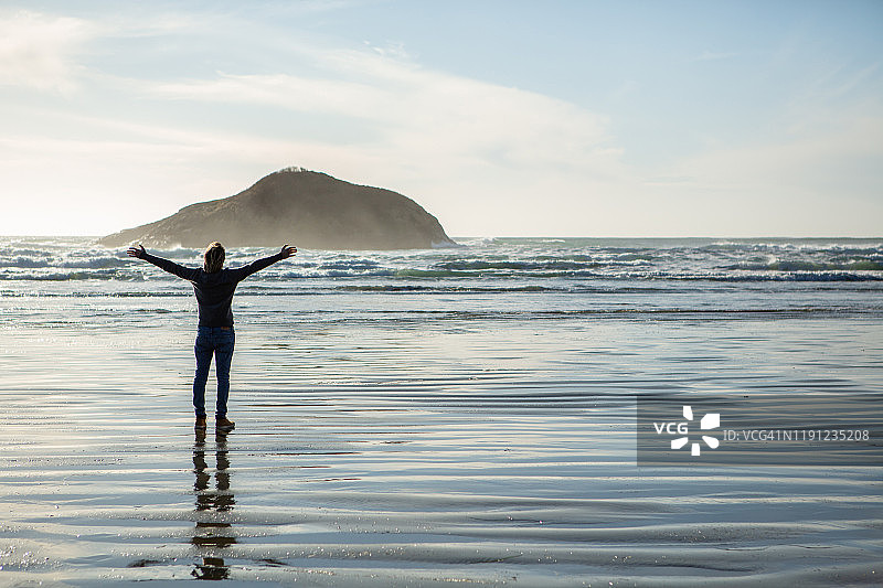 站在海滩上张开双臂拥抱自然的年轻男人图片素材