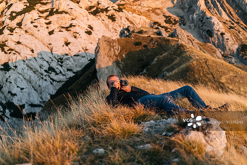 摄影师在日出时躺在草丛中用相机拍照图片素材