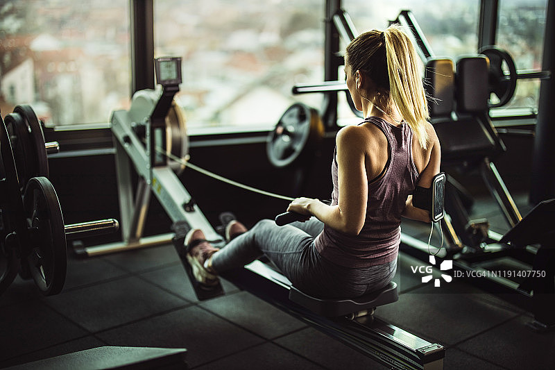健身房内，运动女性在划船机上锻炼并听音乐图片素材