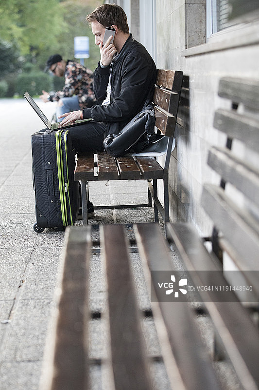 青年男子在巴士站使用手机和笔记本电脑图片素材