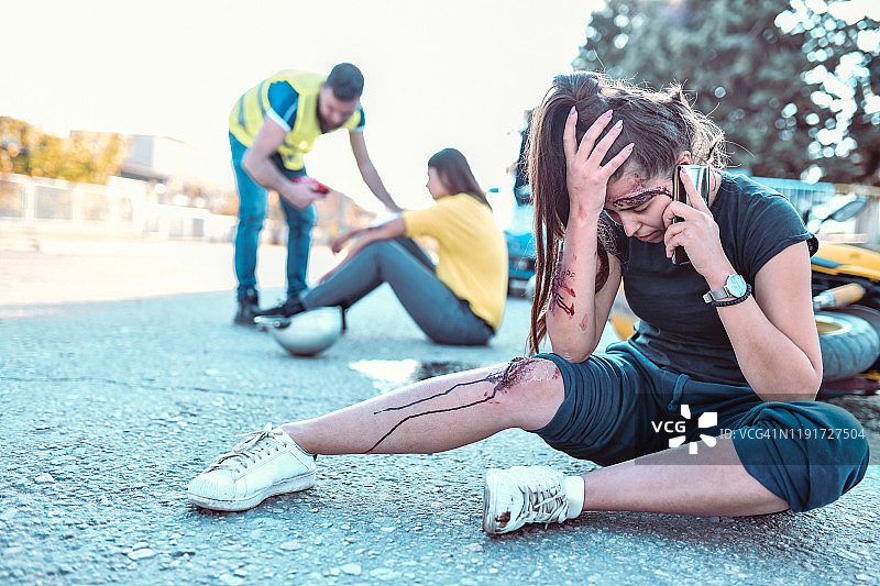 女性在护理人员帮助朋友处理摩托车事故时报警图片素材