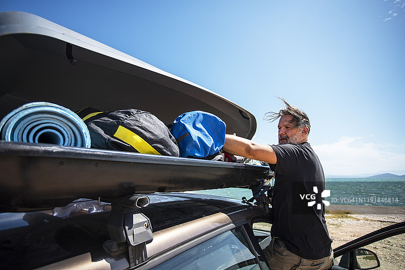 男人在车顶行李架上装载货物箱，准备度假图片素材
