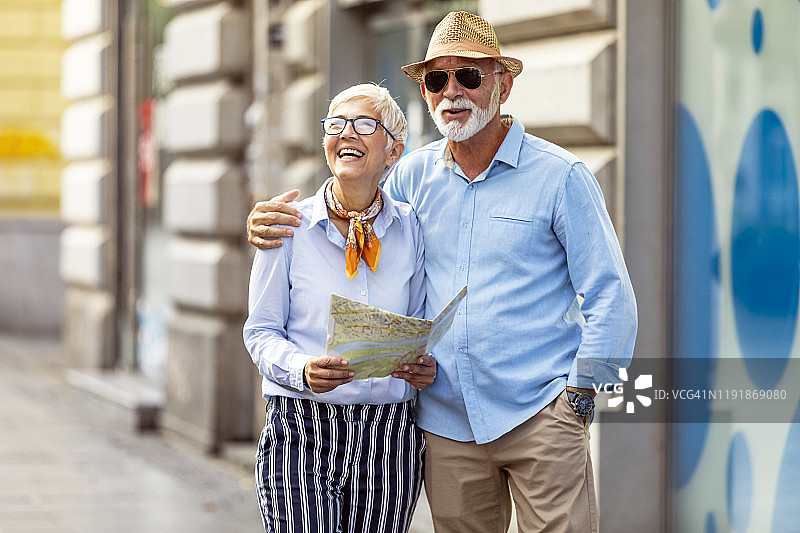 英俊的老年男人和美丽的妻子拿着旅游地图在街上散步图片素材