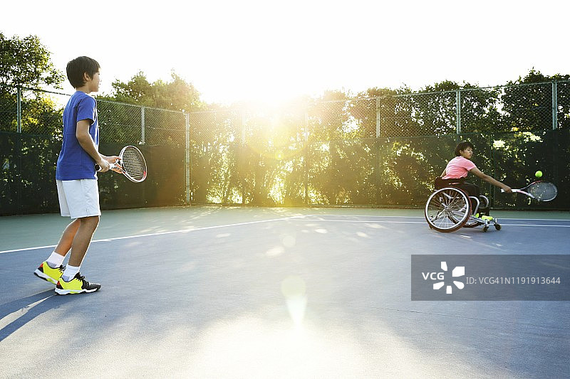 坐在轮椅上的少女和少年在网球场上打网球图片素材
