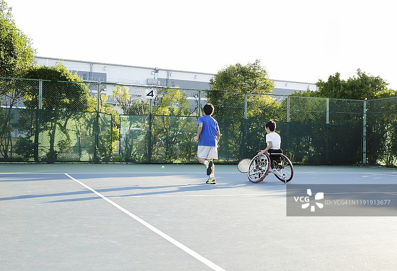 少年与坐轮椅的少年在网球场上跑步的背影图片素材