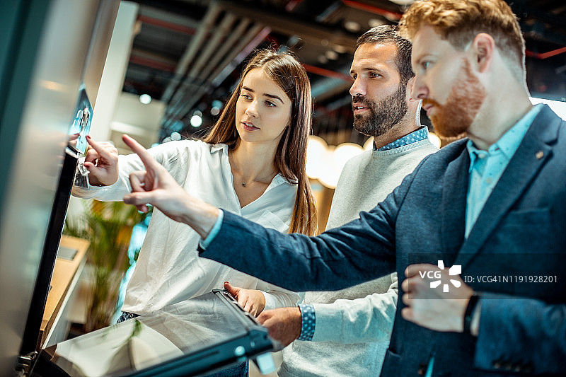 在厨房设备商店里，年轻情侣在售货员的帮助下了解模块化烤箱的烹饪选项图片素材