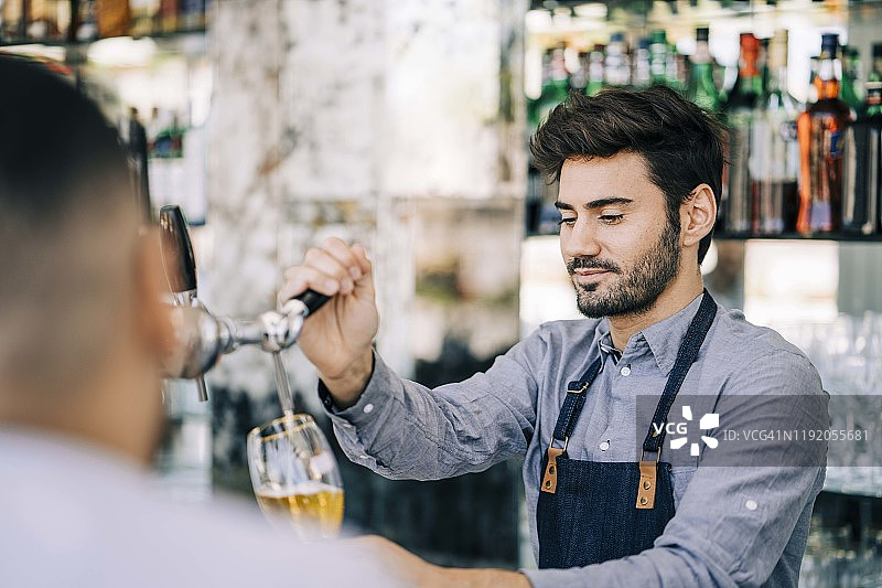 自信的调酒师往玻璃杯里倒啤酒图片素材