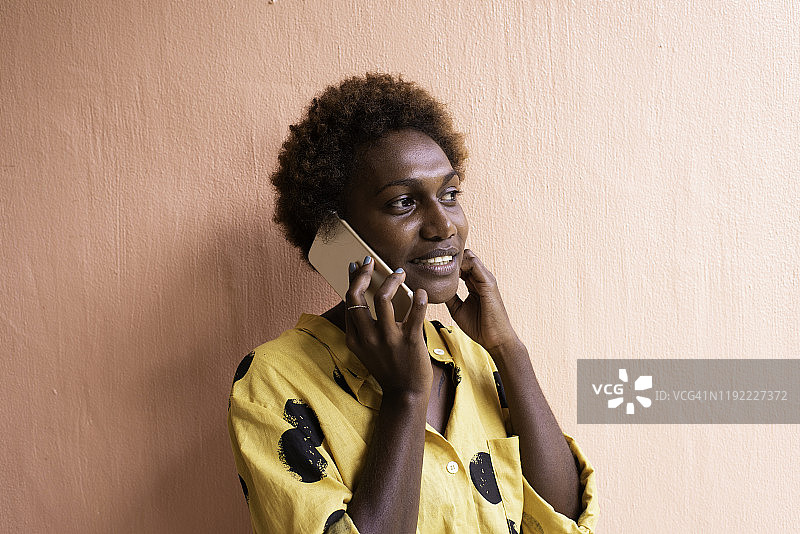 在粉色墙前用手机微笑的年轻女子图片素材