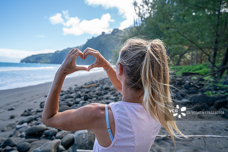 徒步旅行的女人在海岸线上用手比心图片素材