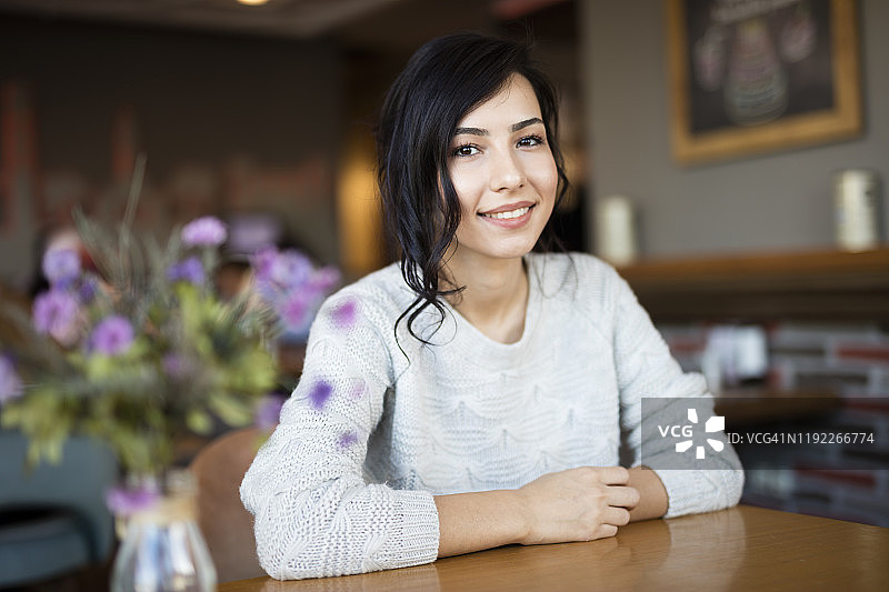 年轻漂亮的女人坐在咖啡馆的桌子旁，看着镜头微笑图片素材