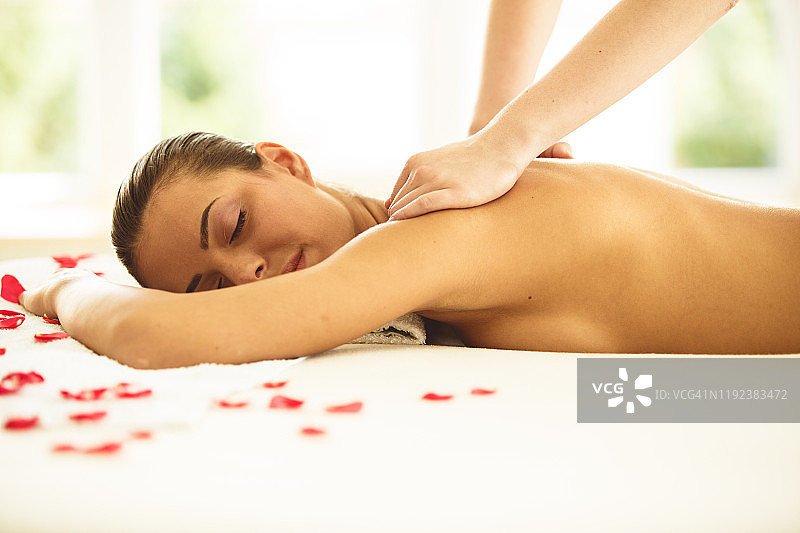 在水疗中心享受玫瑰花瓣按摩的女人图片素材