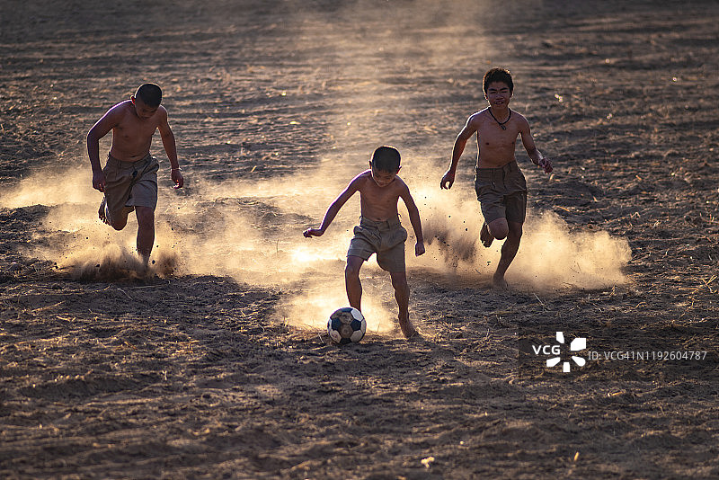 在泥地上踢足球的亚洲男孩图片素材