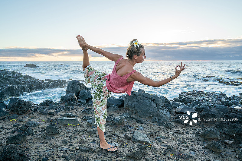 年轻女人在日出时于海边岩石上练习瑜伽图片素材