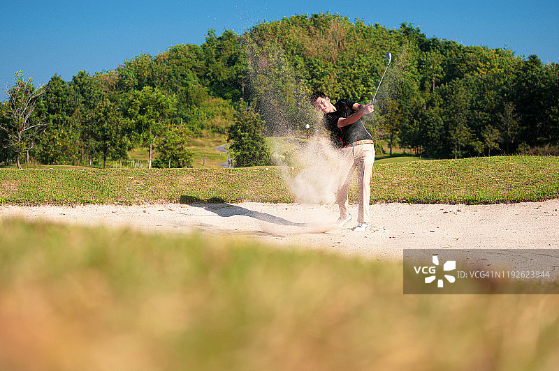 亚洲高尔夫球手从沙坑中击球图片素材