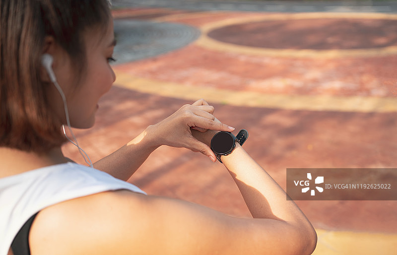 女士们设置跑步健身智能手表。年轻的健身跑步者查看智能手表的时间。年轻女子在公园慢跑时检查心率。图片素材